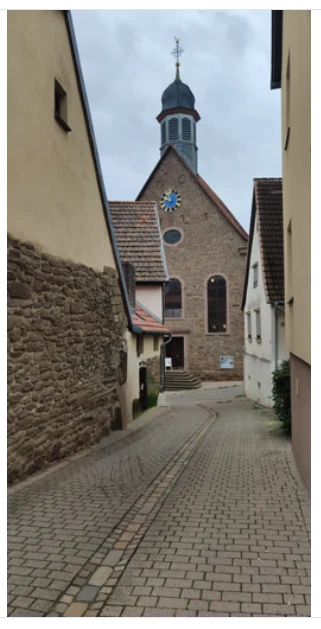 Street photo of a cobbled lane leading to a small church with a clock, after a person was removed by inpainting.